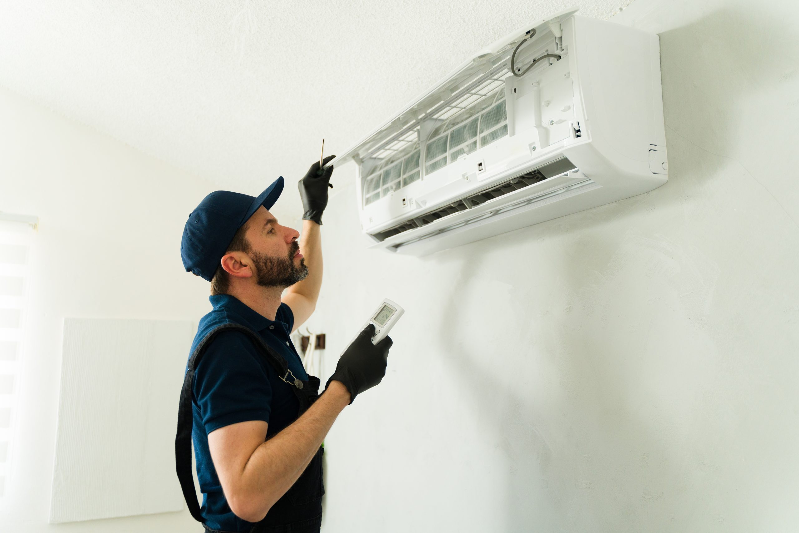 Profile view of hvac technician working on an air conditioning unit, using a remote control and wearing gloves and uniform