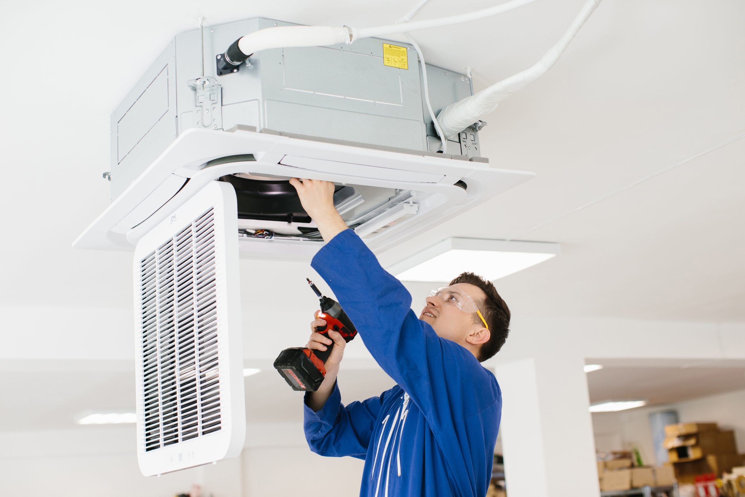 Hvac technician wearing safety glasses and using electric drill while installing air conditioner unit